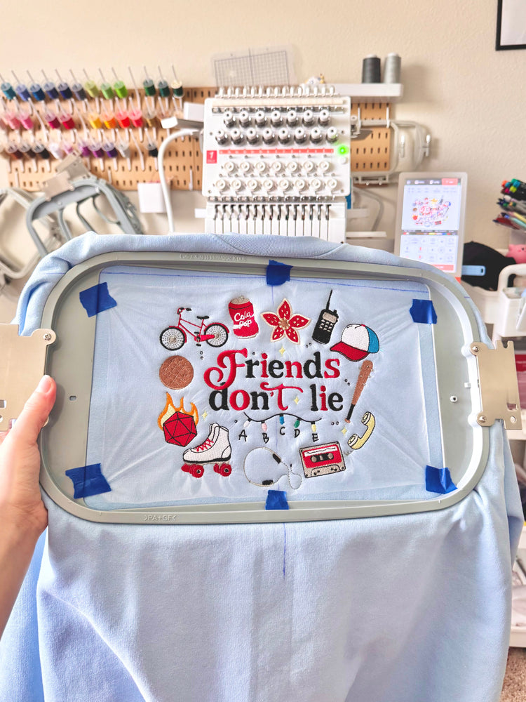 A sweatshirt hooped on the Sewtaku embroidery machine in front of a wall of thread
